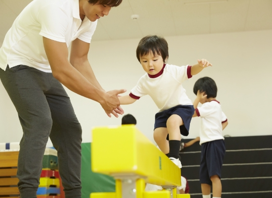 男の子が先生と一緒に平均台に登っている写真